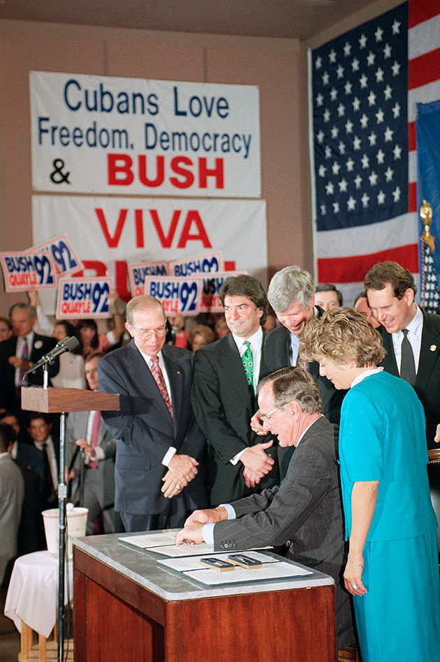 U.S. President George H. Bush signs legislation in Miami, Friday, Oct. 23, 1992 that will tighten the embargo on Cuba. The President is surrounded by supporters in Miami as he signed the bill that he said would "speed the inevitable demise of the Cuban Castro dictatorship." President Bush made an "Ask George Bush" television question and answer appearance following the ceremony at a local TV station.