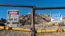 With heaps of rock in the background, signs on a gate read "Abandoned Uranium Mine, Keep Out" with the symbol for radioactivity.