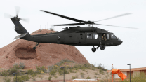 A Black Hawk helicopter takes off against a rust colored desert backdrop.