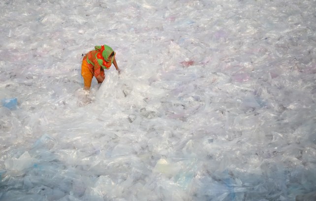 A woman in bright orange hunches over a sea of white and grey plastic bags. 