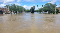 Flooding showing trees, cars and parts of building submerged in water, the sky is blue