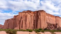 A big orange rock formation in front of a cloudy sky.