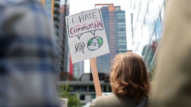 A person with golden-brown hair holds a sign that says "I hate commuting."