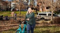 Luchia holds her blue electric bike in her lawn on a fall day.