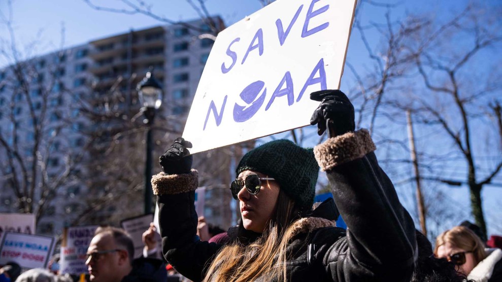 A person with long dark hair holds up a sign that says "Save NOAA"