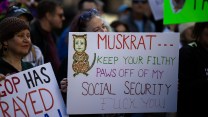 A woman with a sign at a protest that says, "Muskrat. Keep Your Filthy Paws Off My Social Security. Fuck You."