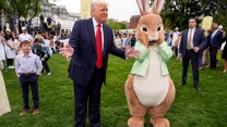 Donald Trump stands next to a person in an Easter Bunny costume on a lawnl The Easter Bunny is holding its hands up to its face.