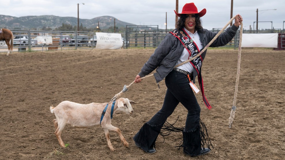 Person in red cowboy hat, pageant-style sash, and fringed black pants leading a goat on a leash.