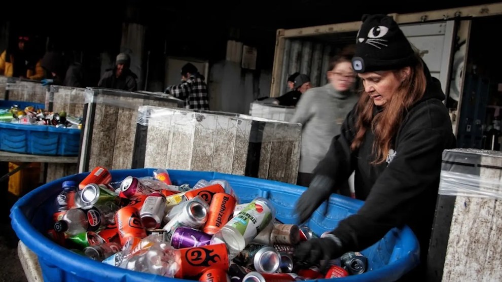 A person places cans into a blue tub
