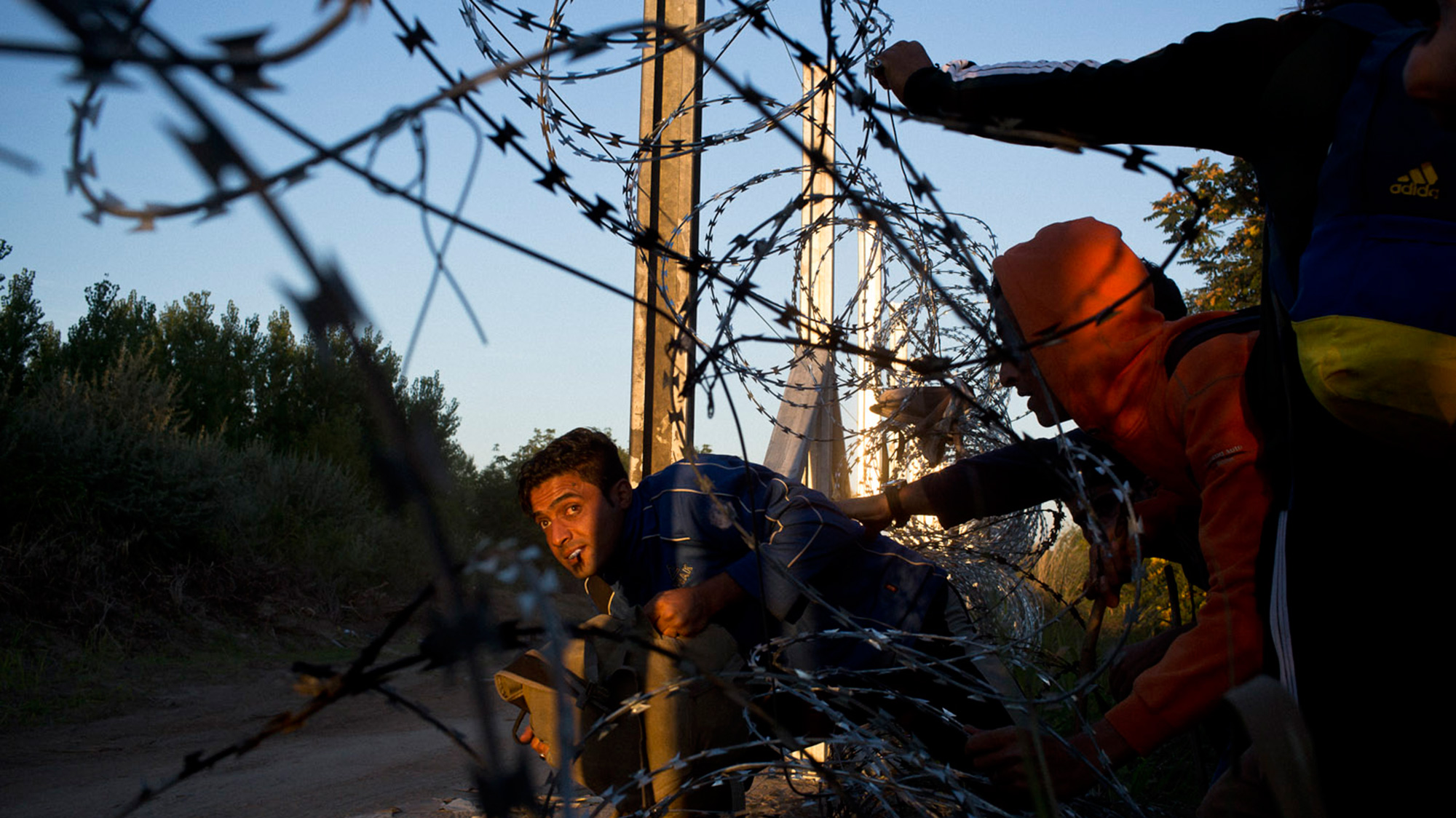 Refugees crossing through barbed wire fence.